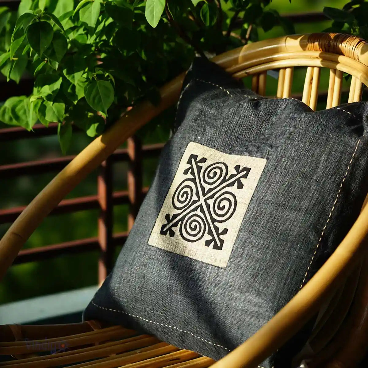 Handgjort grått hampakuddfodral med svart tribalruta i trädgårdsmiljö