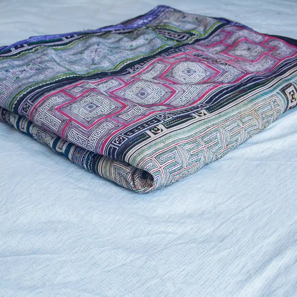Vindigo dual-sided cotton bed cover folded showing Hmong embroidery and batik sides