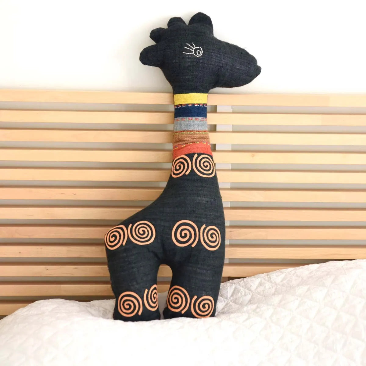 Side view of spiral embroidered deer plushie sitting on bed