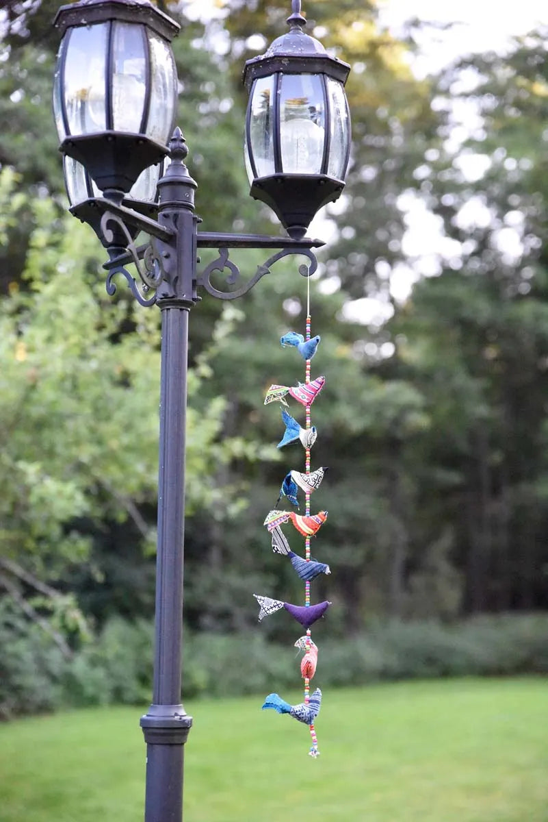 Tygfåglar i olika färger hänger vid svart gatlykta i kvällsljus