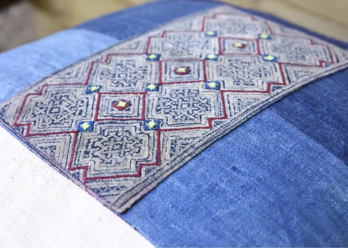 Handbroderade mönster i grått tribaltyg på blå kuddbaksida