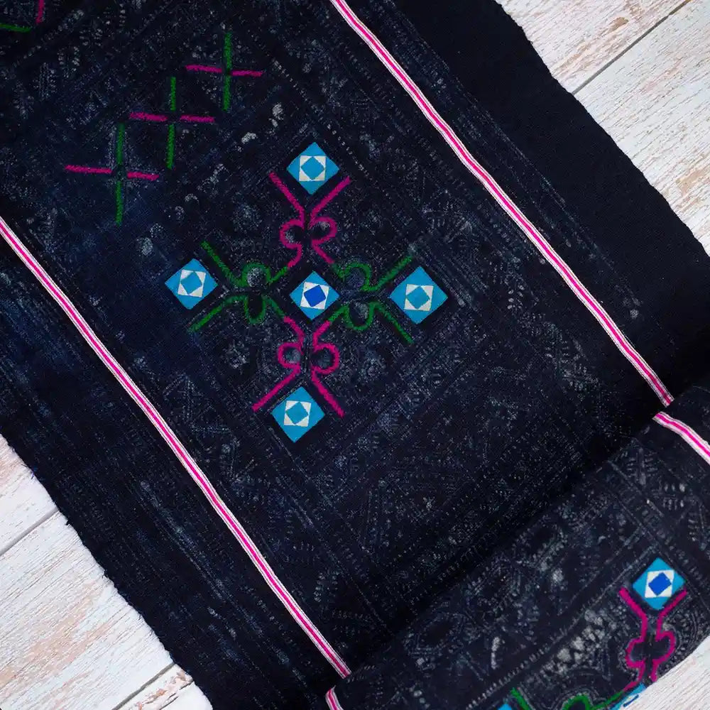 Top-down view of vintage Hmong black fabric with glowing blue square and pink border