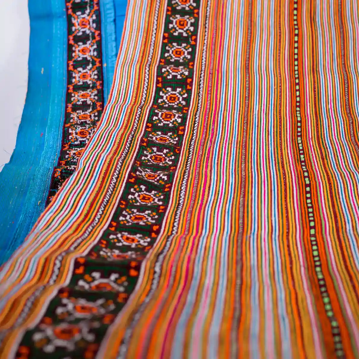 Vindigo striped orange cotton fabric roll showing floral embroidery edge