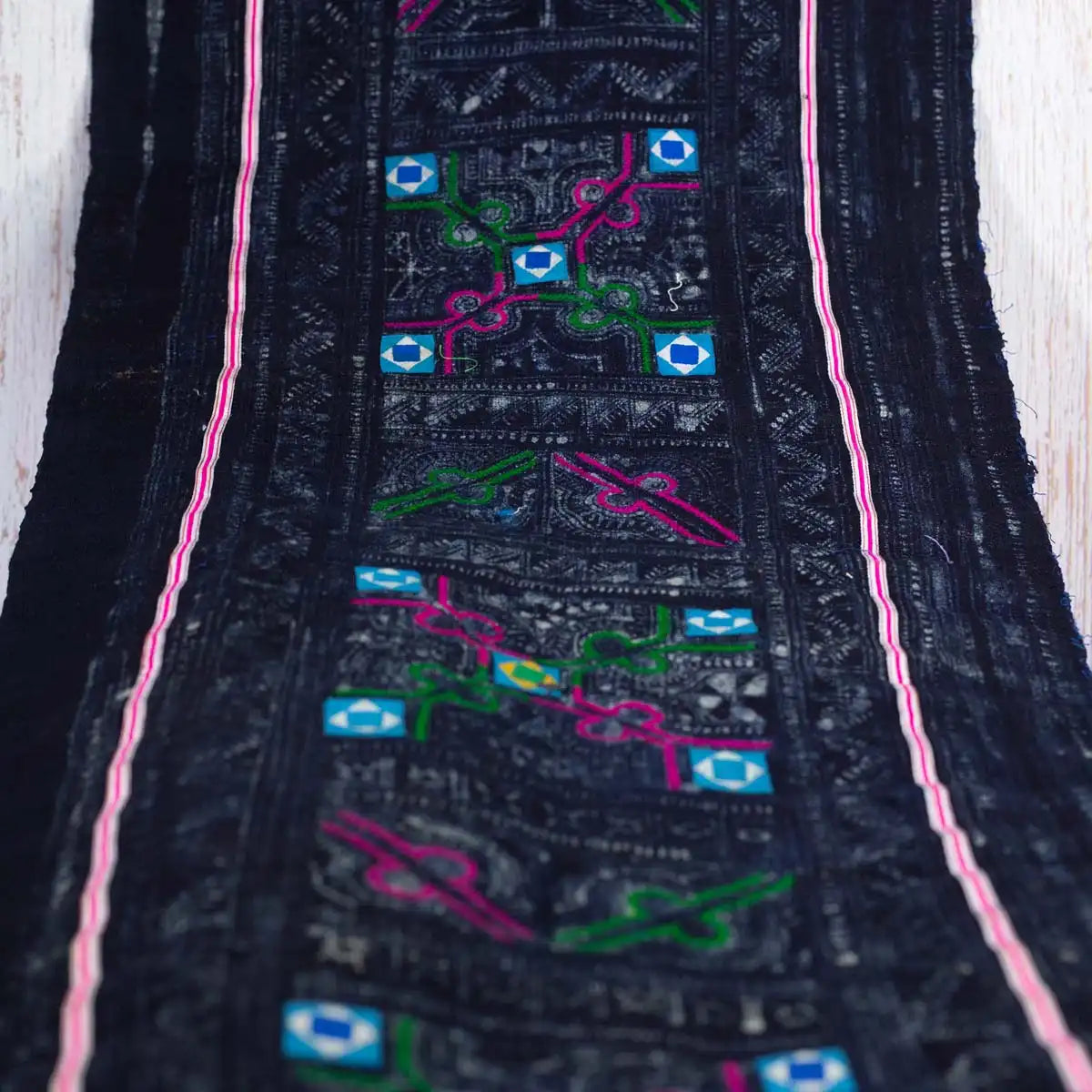 Top-down view of Vindigo black embroidered fabric roll with colorful motifs and pink border