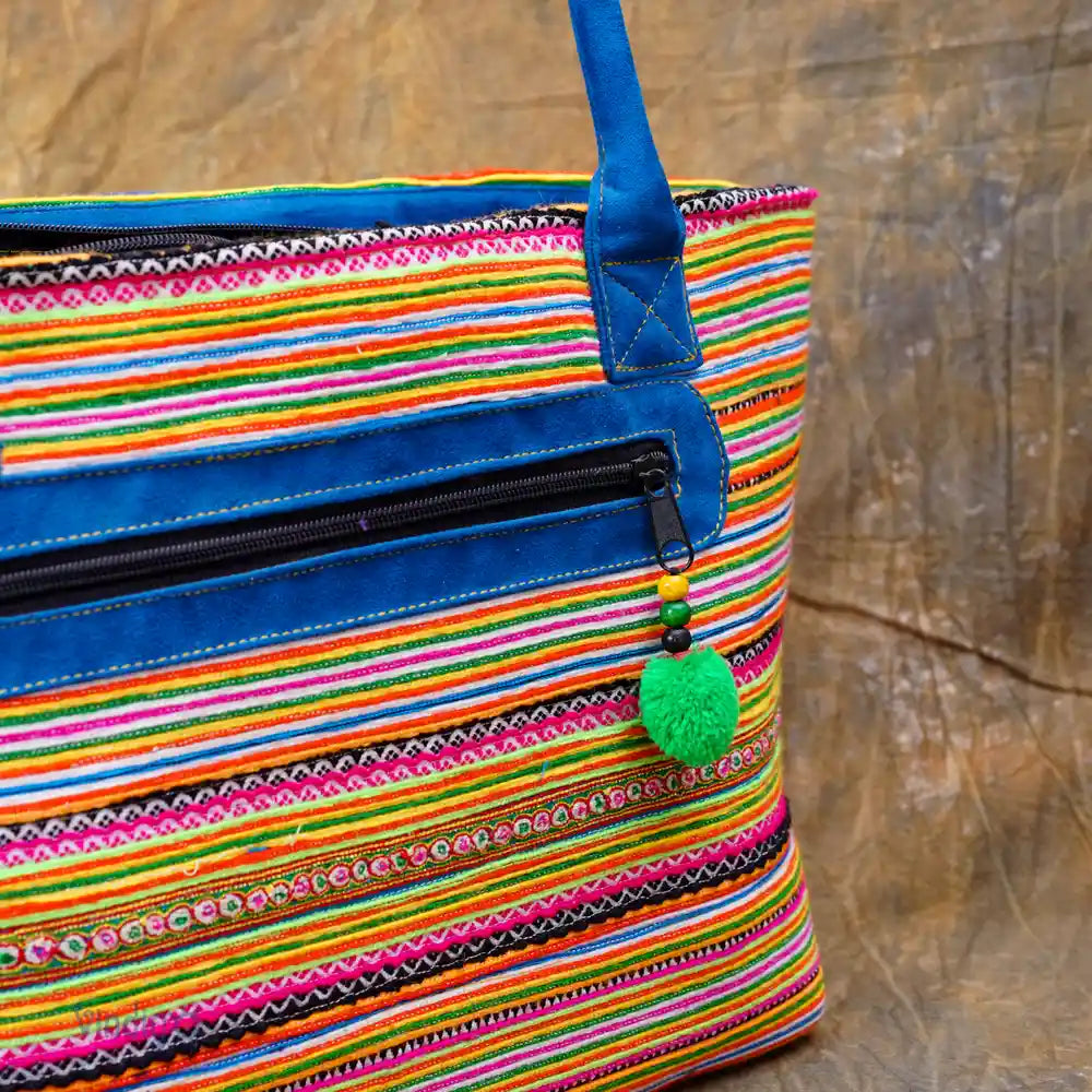 Närbild på dragkedja och grön pompom på färgglad tribaltygväska