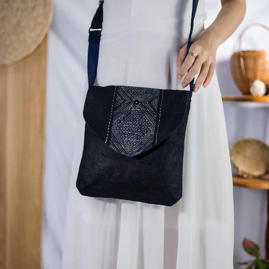 Model carrying black hemp crossbody bag with long strap and H’Mong patch, sustainable fashion.