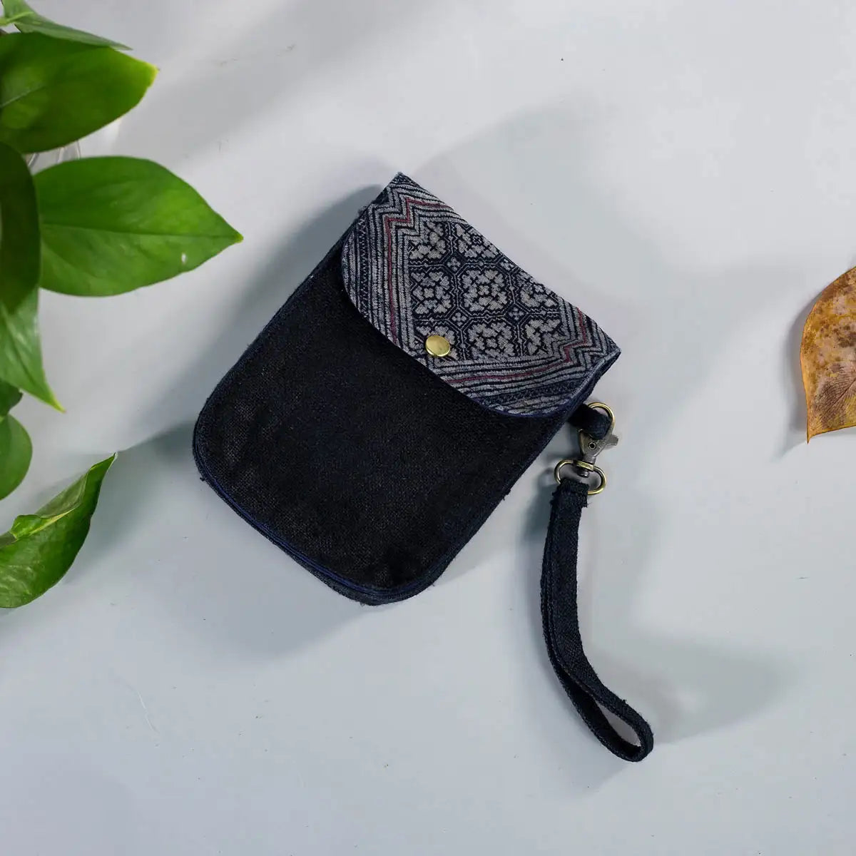 Flatlay of black hemp flip phone belt bag with H’Mong patch, eco-friendly handmade accessory.