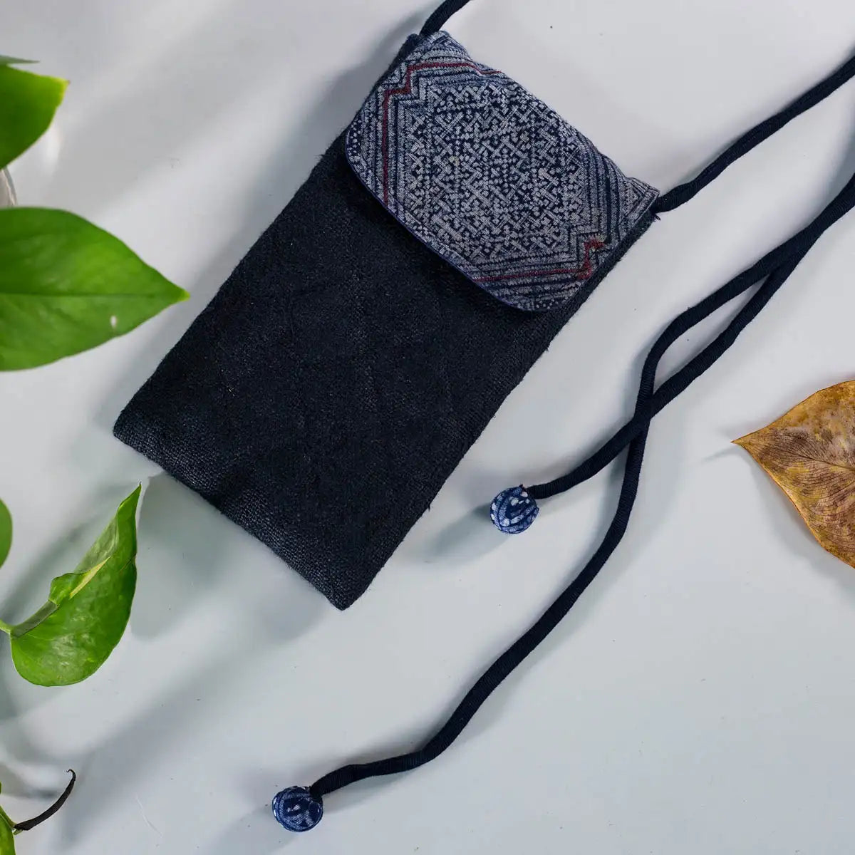 Flatlay of black hemp phone bag with H’Mong patch, handmade eco-friendly design with adjustable strap.
