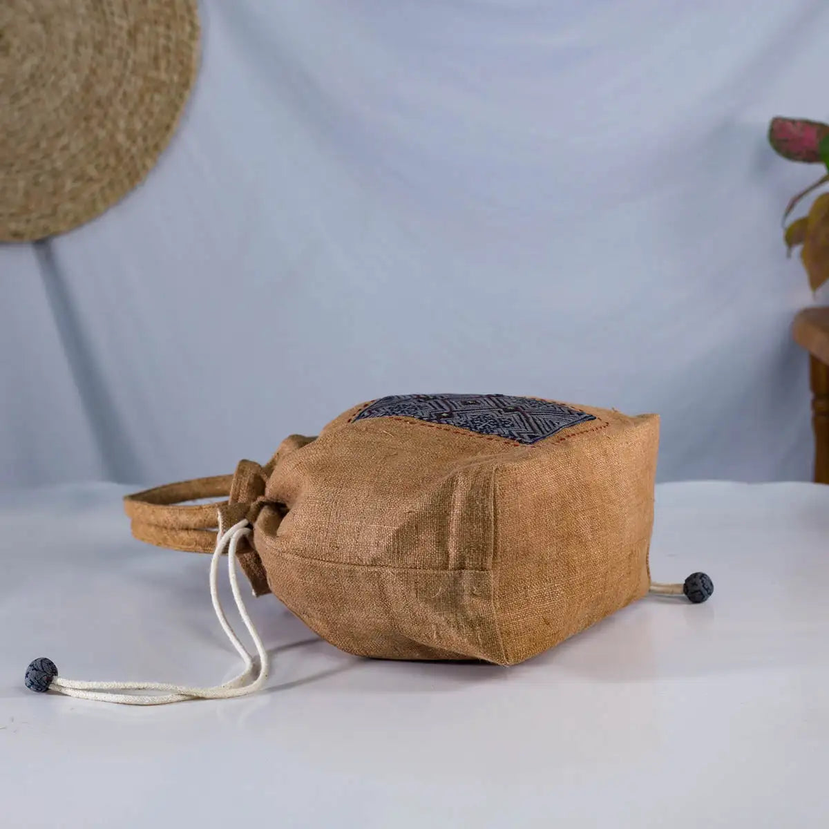 Side view of natural hemp bucket bag with H’Mong patch and round handles, eco-friendly fashion.