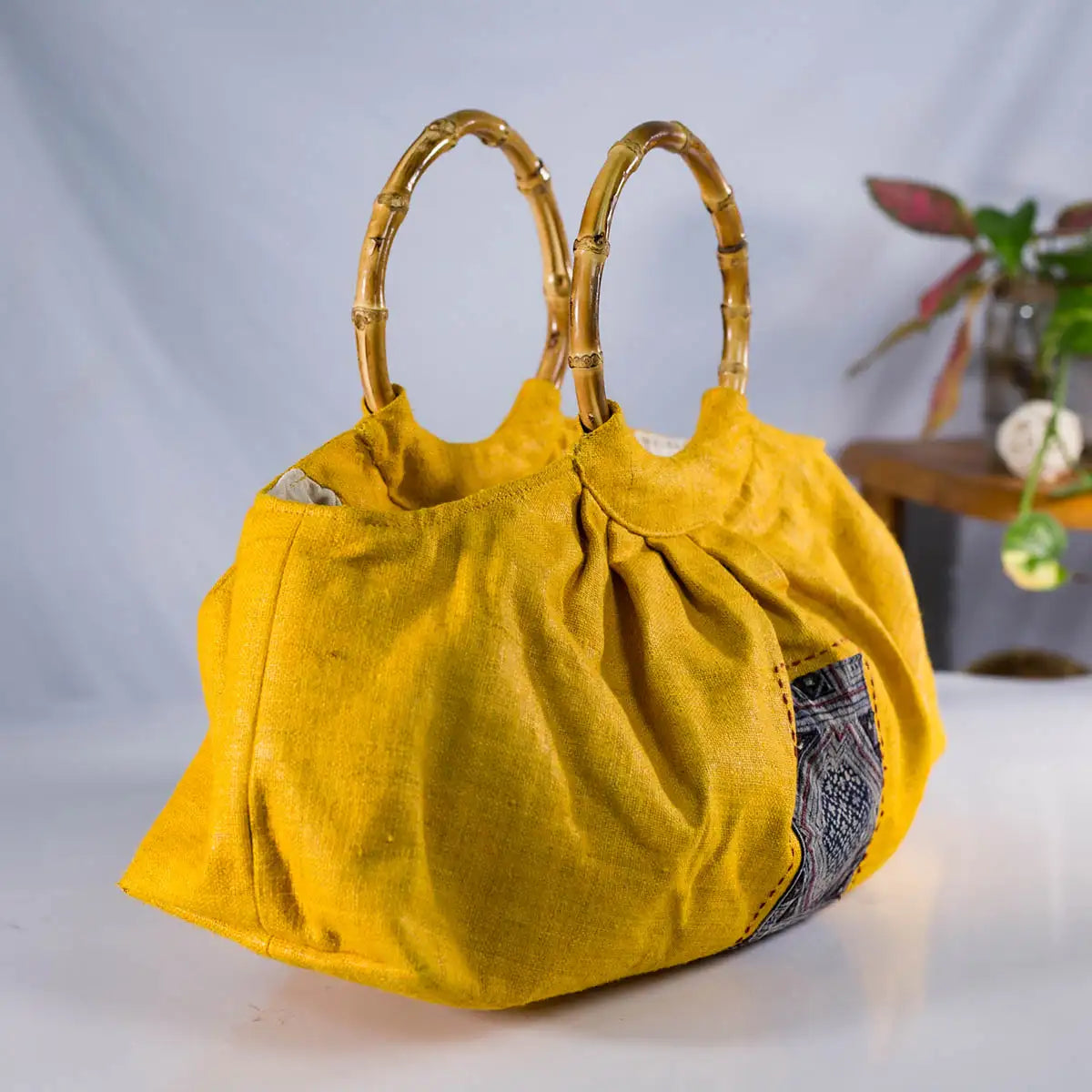 Back view of handmade yellow hemp handbag with bamboo handles and patchwork accent.