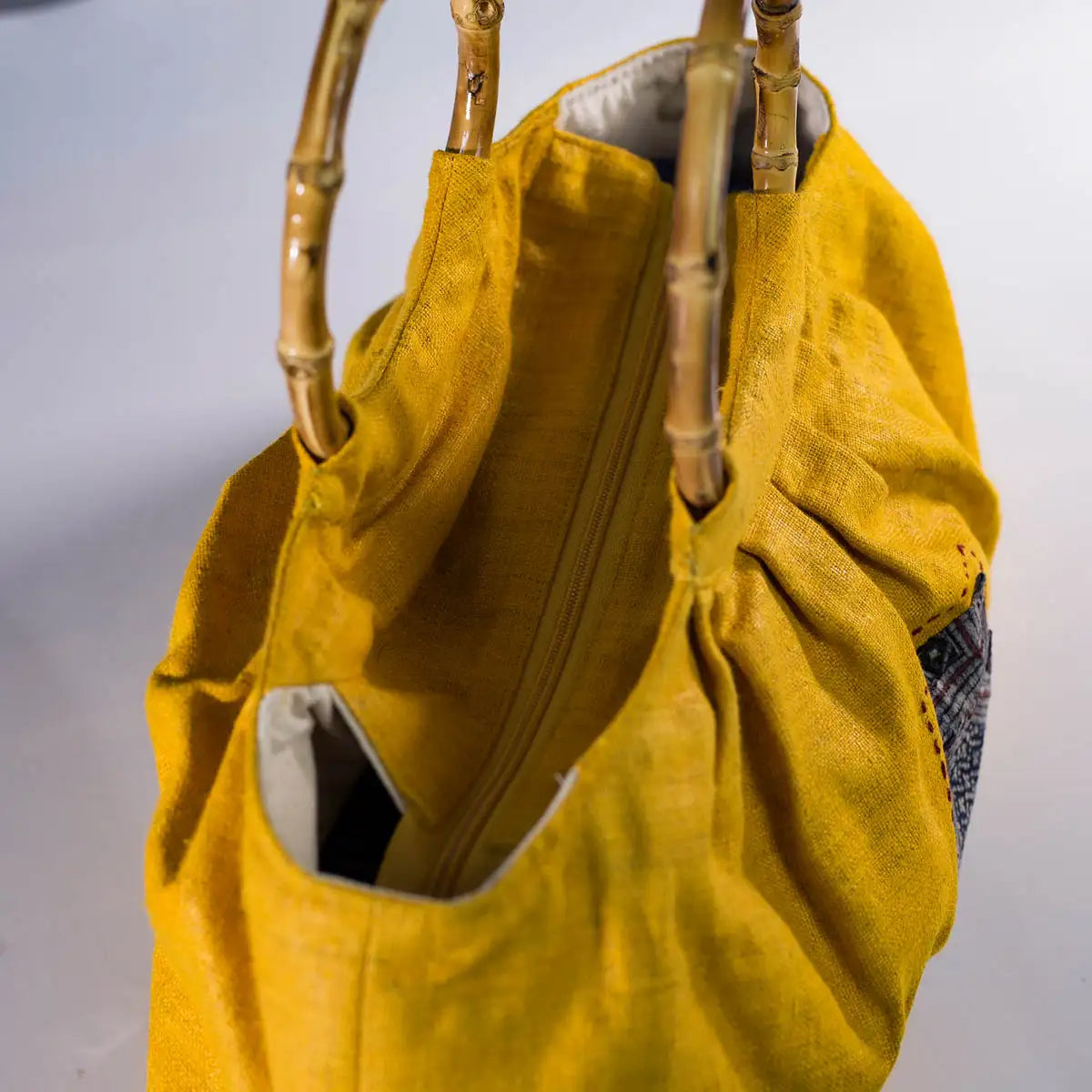 Side view of yellow hemp handbag with bamboo handles and indigo fabric pocket.