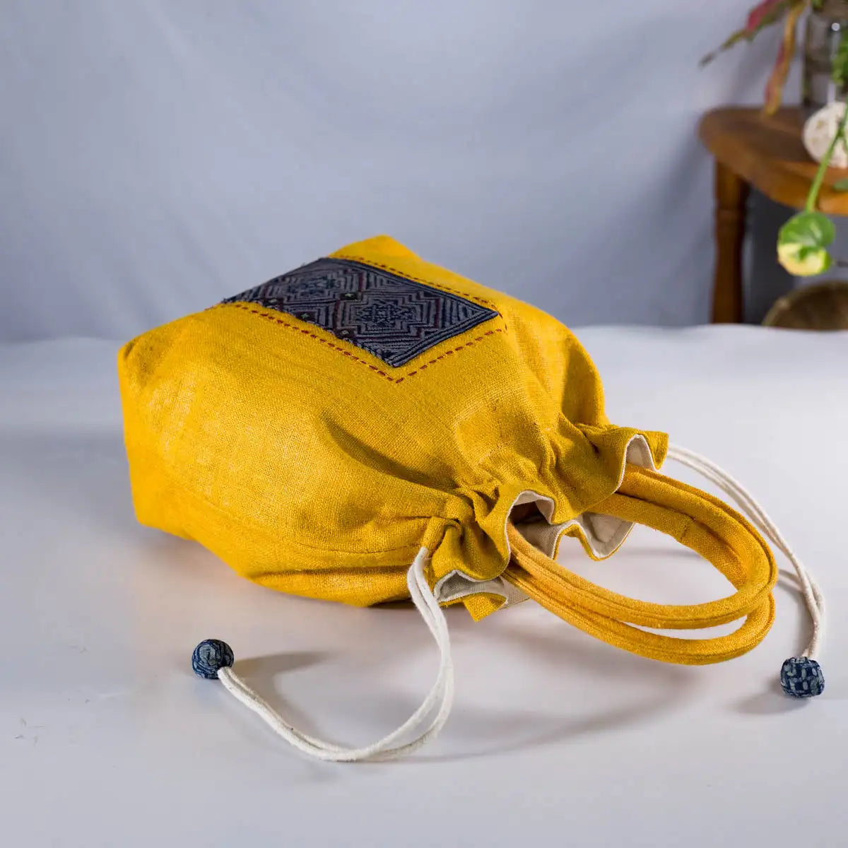 Handmade yellow hemp drawstring bucket bag by Vindigo shown from side view with embroidery detail.